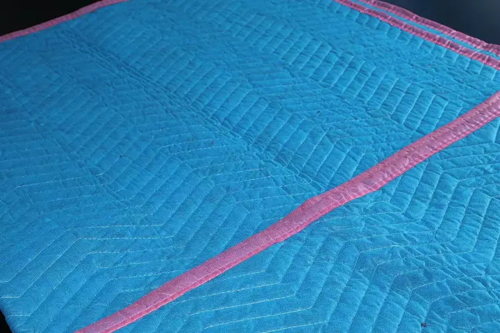 Baby blue cotton moving pad laid flat with pink trim